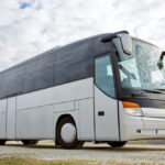 Un autocar de tourisme moderne et blanc stationné sur un terrain dégagé, illustrant comment obtenir un devis pour la location d'un autocar.