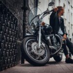 Un homme en veste de cuir pose à côté de sa moto cruiser style chopper dans une rue de la ville.