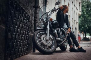 Un homme en veste de cuir pose à côté de sa moto cruiser style chopper dans une rue de la ville.