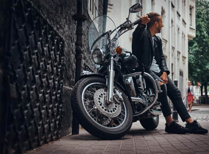 Un homme en veste de cuir pose à côté de sa moto cruiser style chopper dans une rue de la ville.