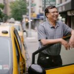 Un homme souriant repose la main sur la portière d'un taxi