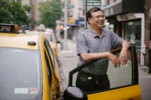 Un homme souriant repose la main sur la portière d'un taxi