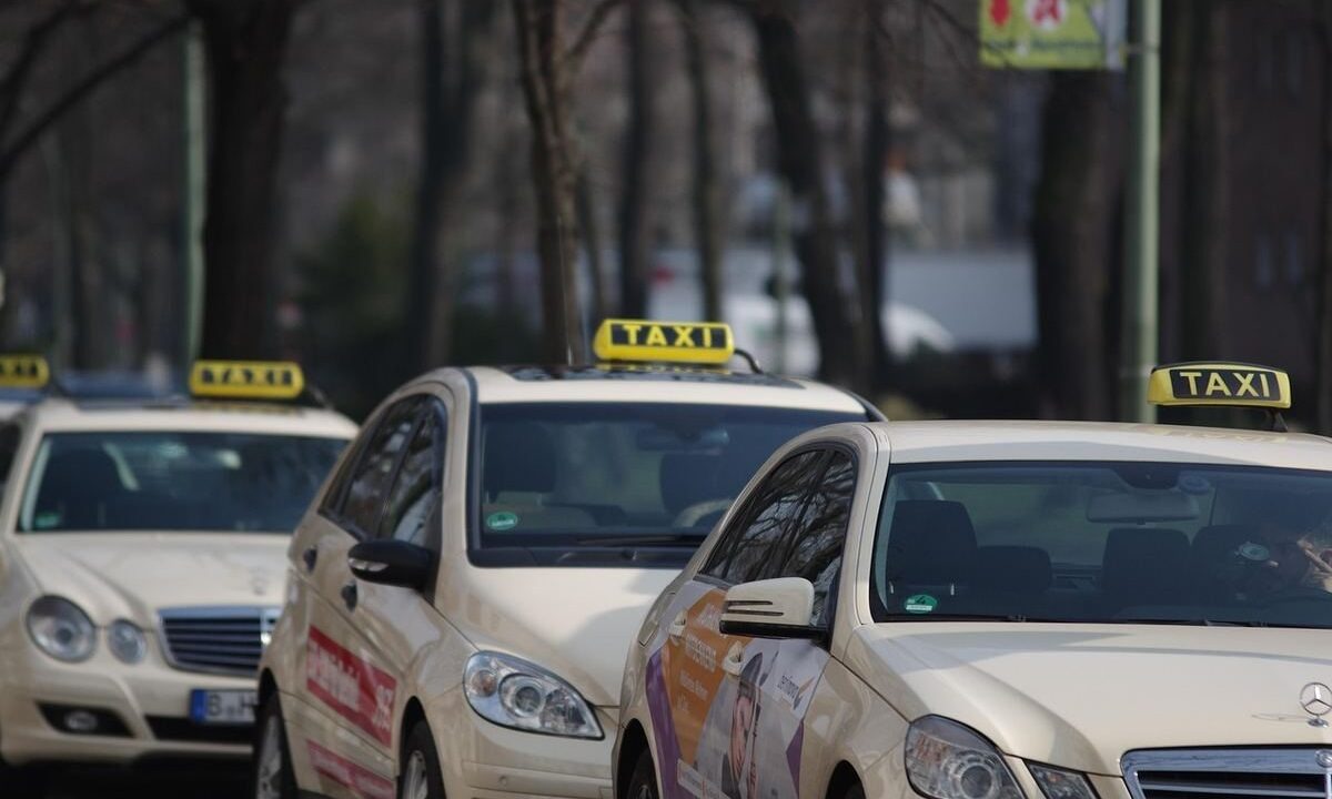 Des voitures-taxis alignées sur une rue, panneaux lumineux visibles