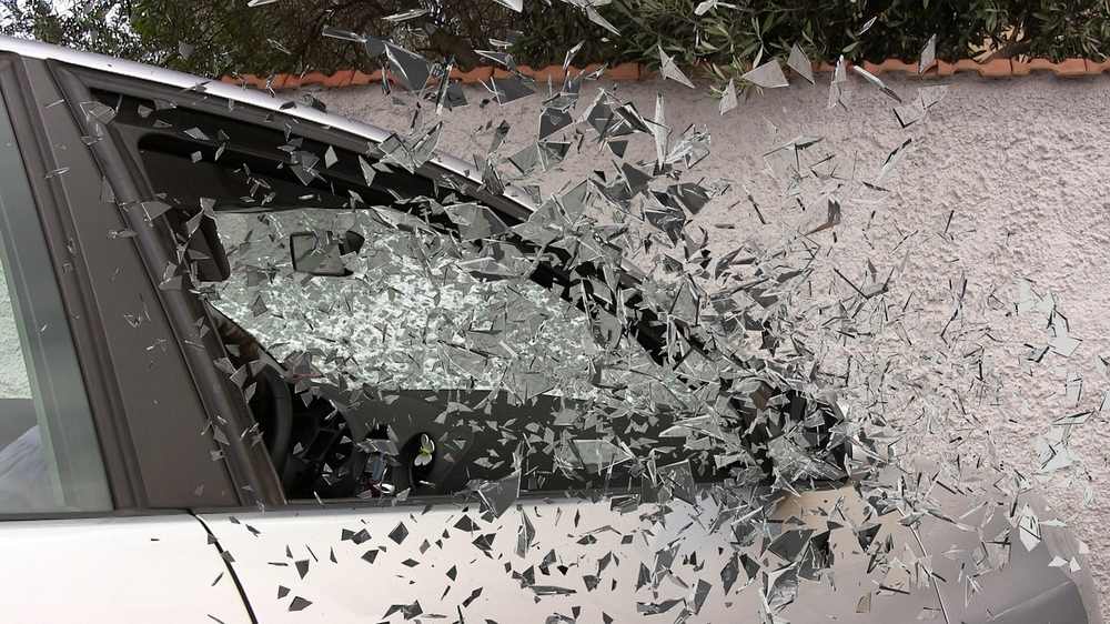 Vitre de voiture explosée, éclats de verre en vol, mur en arrière-plan