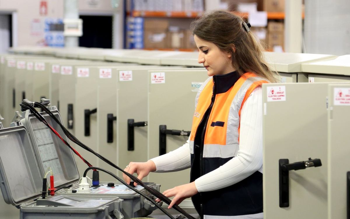 Technicien en gilet orange manipule des câbles près d'un coffre gris dans un entrepôt
