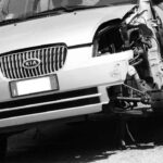 Voiture Kia blanche après choc frontal, moteur visible, roue avant droite absente